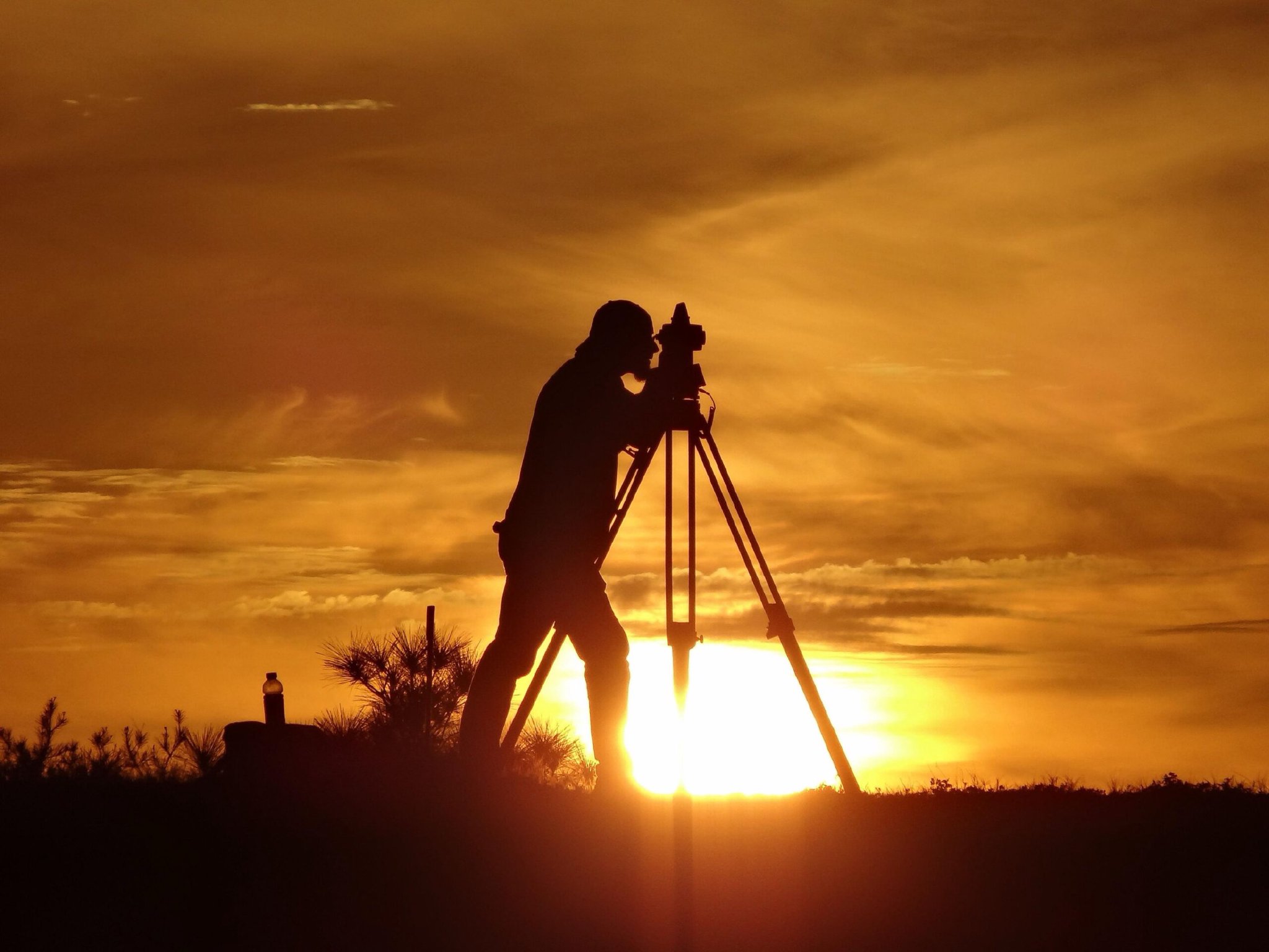 Surveyor at a tripod on open land at sunset